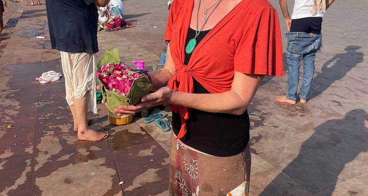 A person holding a floral offering at a riverside.