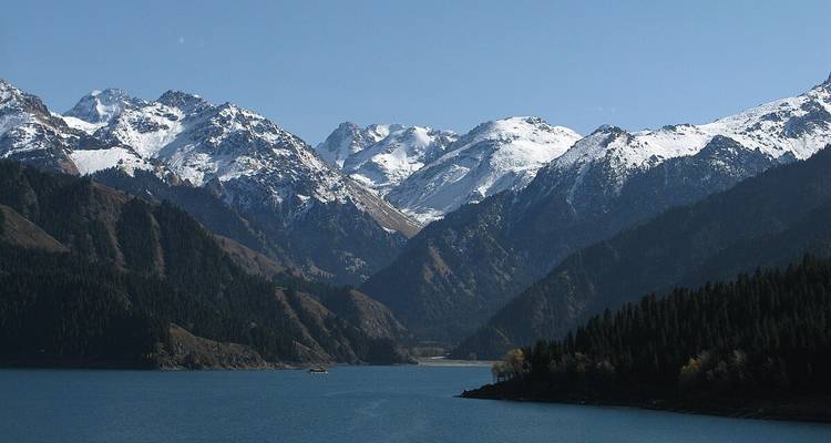 Snow-capped mountains with a calm lake in the foreground.