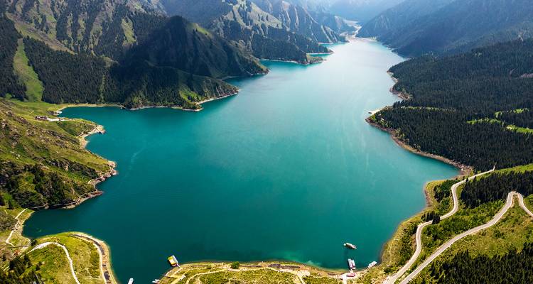 Aerial view of a lake surrounded by mountains and winding roads.