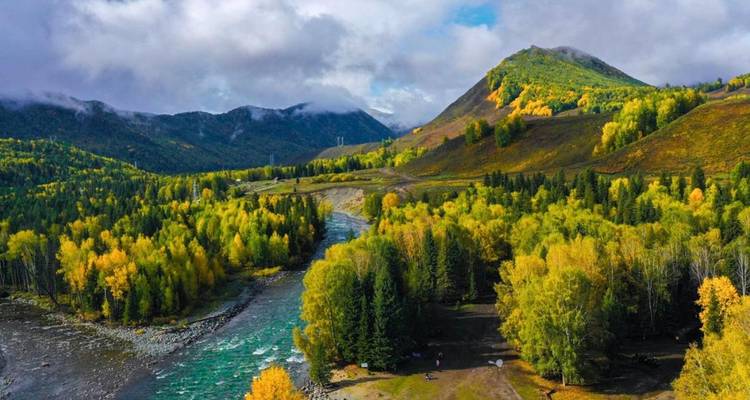 Vibrant autumn landscape with a river and lush forested hills.