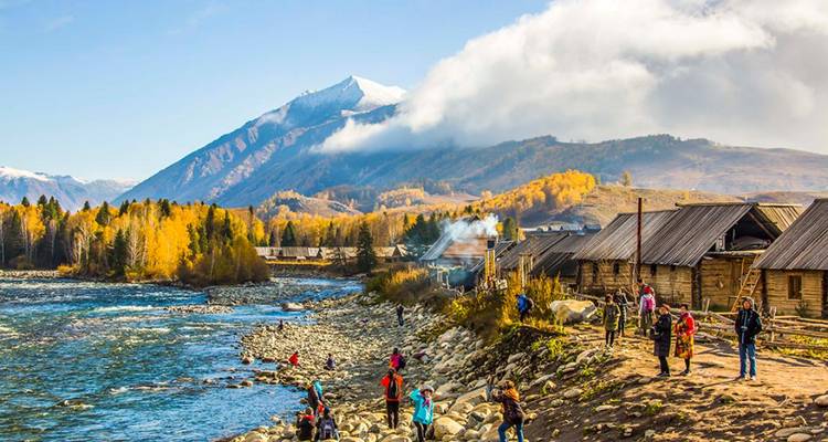 People by a riverside village with mountains in the background.