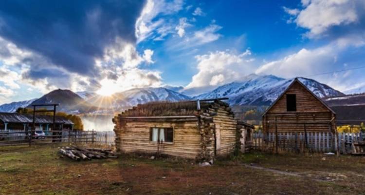 Wooden cabin with snowy mountain backdrop during sunrise.