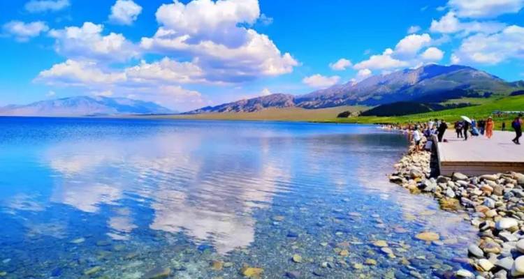 Landscape with people along a lakeshore and a reflection of clouds.