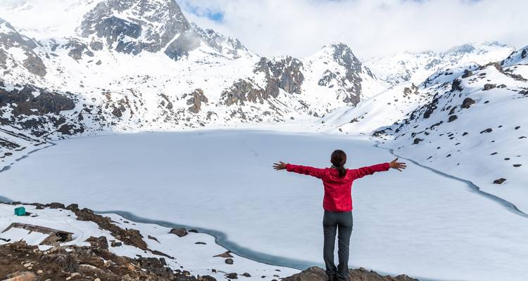 Person, die mit ausgestreckten Armen vor einem schneebedeckten See steht.