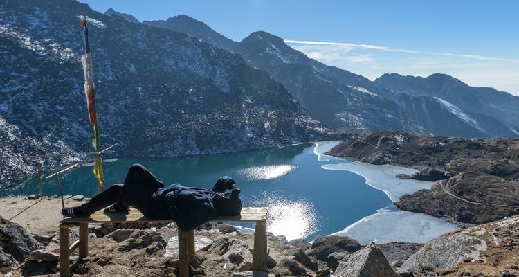 Person, die auf einer Bank entspannt und auf einen bergigen See blickt.