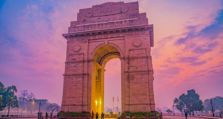 El monumento India Gate brillando contra un cielo de amanecer en tonos pastel con los primeros visitantes en primer plano.