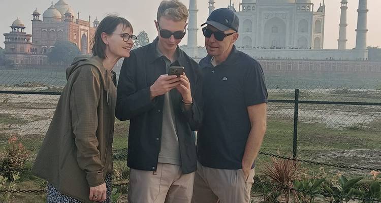 Trois personnes regardant un téléphone devant le Taj Mahal.