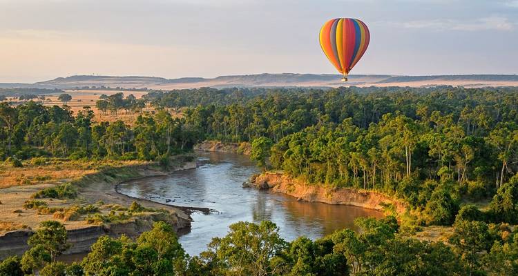 Un globo aerostático flotando sobre un río y un frondoso bosque verde.