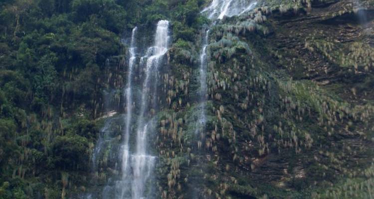 Een waterval die naar beneden stort langs een weelderige groene bergwand.