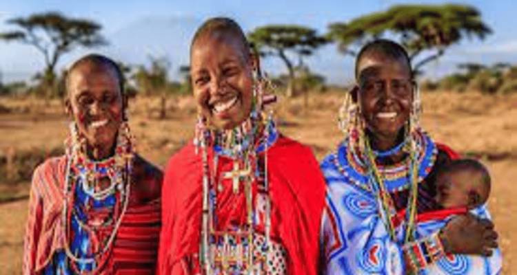 Trois femmes en tenue traditionnelle souriant dans un paysage rural.