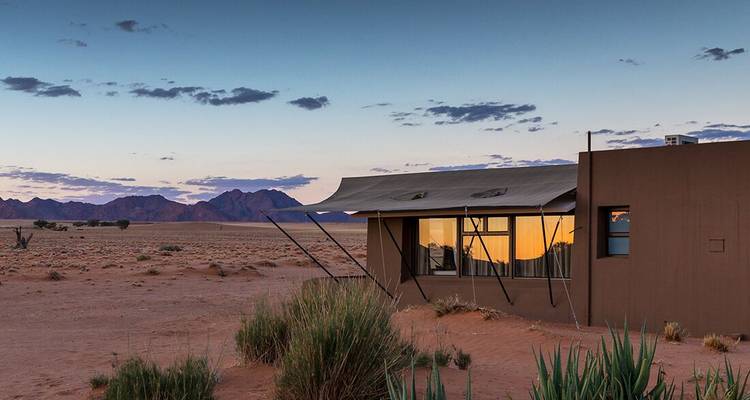 A modern building in a desert setting at sunset.