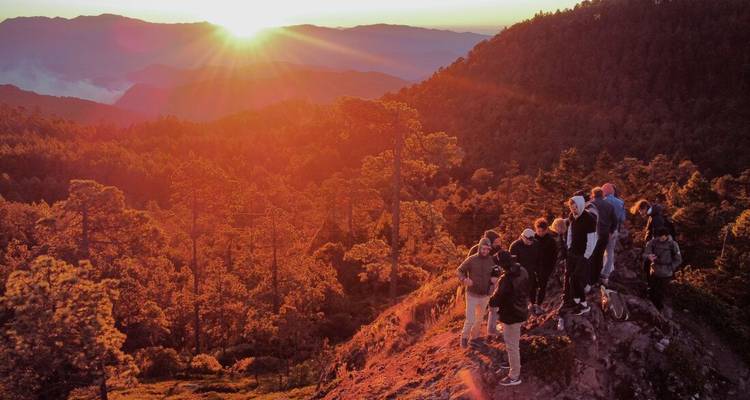 A group of people watching a sunset over a mountainous area.