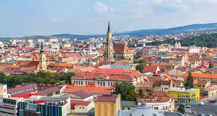 Vue panoramique de Cluj-Napoca avec une église proéminente et les collines environnantes.