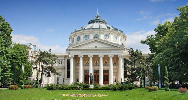 Romanian Athenaeum’s grand domed facade framed by manicured lawns and tall trees on a bright day.