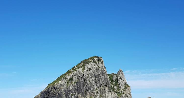 Rugged rock formation against a clear blue sky in a coastal region.