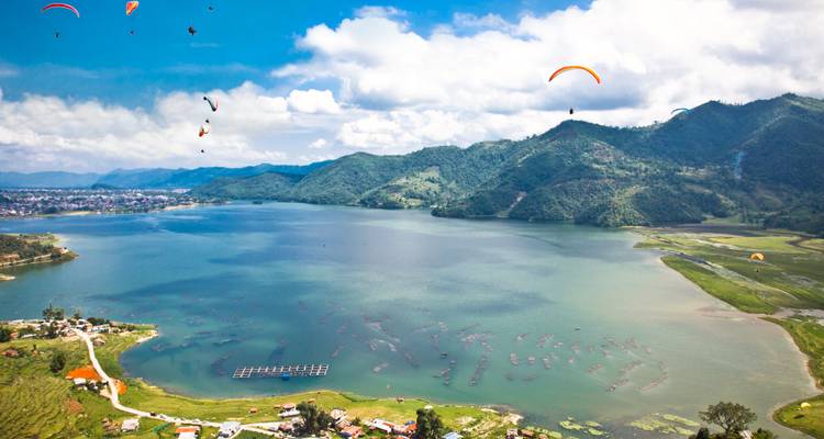 Paragliders over a lake with mountains in the background.