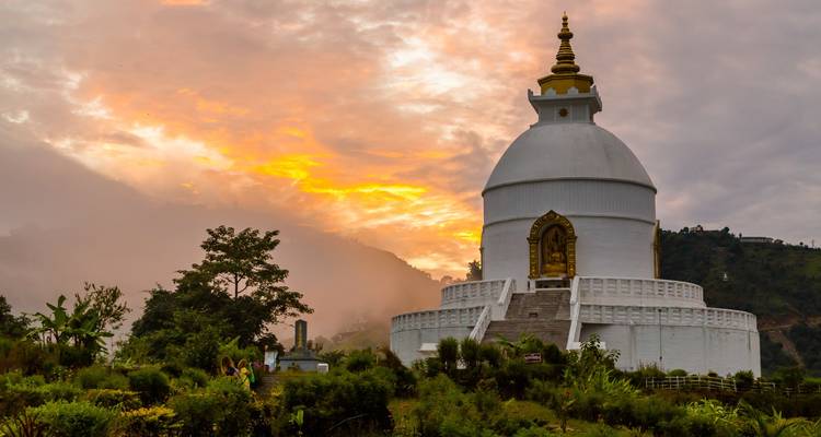 A white stupa on a hillside against a sunset sky.
