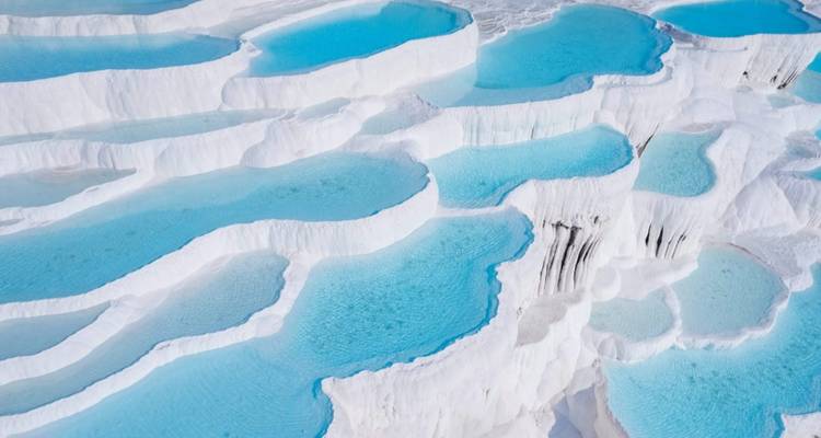 Aerial view of white thermal terraces filled with blue water.
