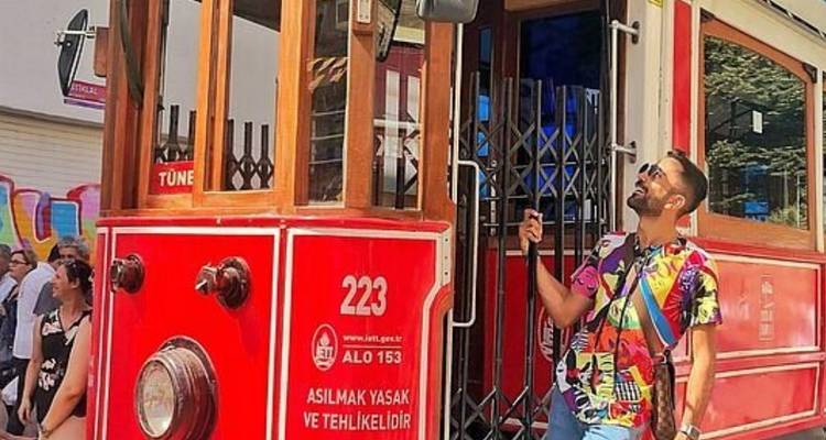 Man posing beside a red vintage tram on a street.