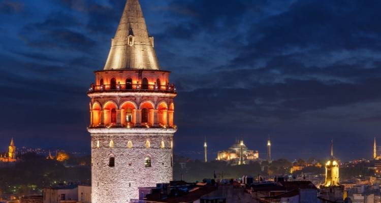 Historic tower lit up at night with other city lights visible.