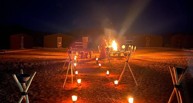 Campement nocturne dans le désert avec feu de camp et torches.