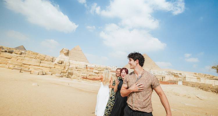 Groupe de touristes posant avec les pyramides en arrière-plan.