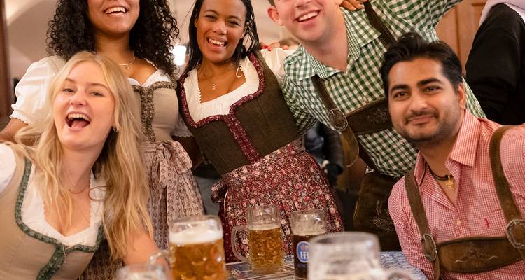 Amigos vestidos con trajes tradicionales bávaros brindan con grandes jarras de cerveza dentro de una animada cervecería