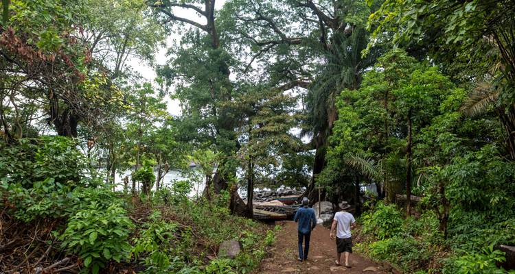 Deux personnes marchant sur un sentier de forêt tropicale luxuriante vers la plage.