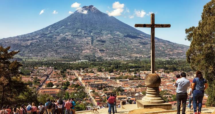 Dominant la ville d'Antigua avec un grand volcan et une croix au premier plan.