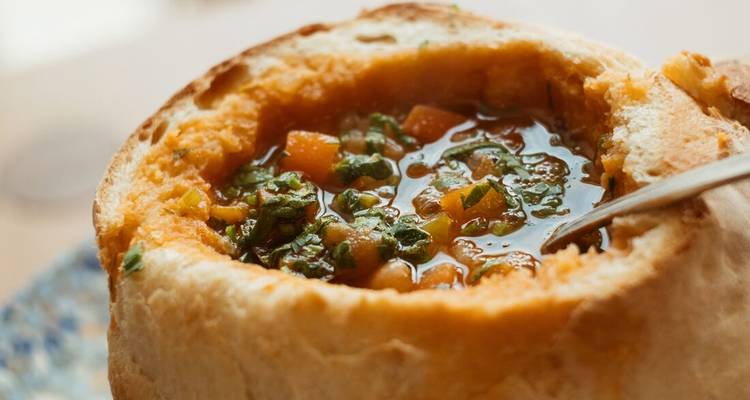 Bowl of soup inside a bread bowl with herbs.