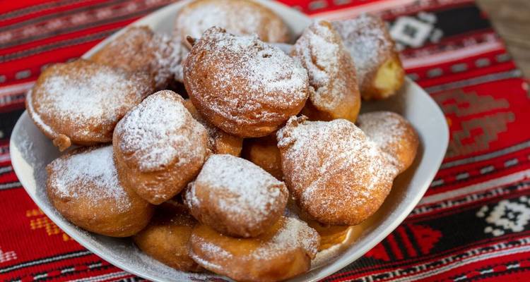 Plate of traditional Romanian donuts dusted with powdered sugar.