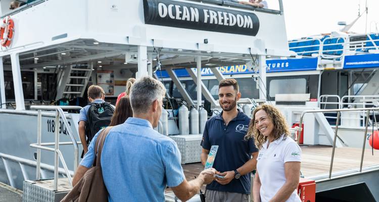 Des gens rassemblés sur un quai avec du matériel de plongée, avec un navire nommé 'Ocean Freedom'.