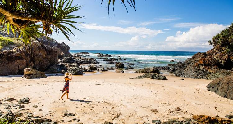 Persona caminando en una hermosa playa de arena con rocas y olas del océano.
