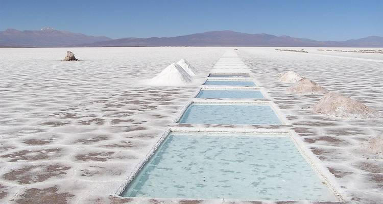 Uitgestrekt uitzicht op de Salinas Grandes zoutvlaktes met stapels zout en bergen op de achtergrond.