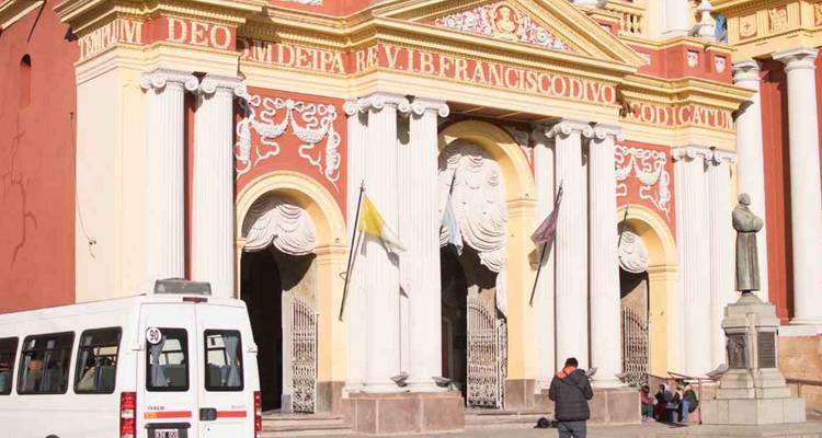 Kerk in barokstijl met mensen die bij de ingang lopen. Een busje geparkeerd buiten.