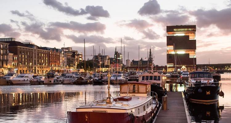 Boote im Hafen bei Sonnenuntergang mit einem modernen Gebäude im Hintergrund.