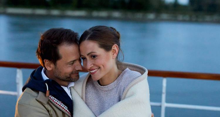 Paar in eine Decke gehüllt, sitzend auf einem Boot mit Flussblick.