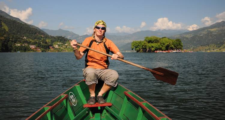 Person rowing a boat on a lake with mountainous landscape.