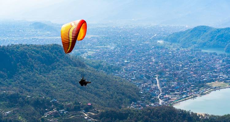 Paraglider soaring above a city with a lake below.