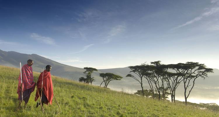 Two Maasai men in traditional clothing walking in a scenic landscape.