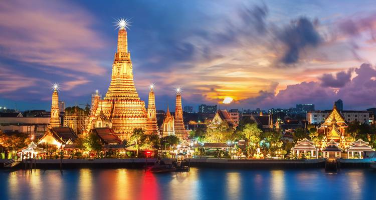 Buddhist temple at sunset with lights reflecting on the river.