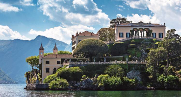 Villa luxueuse au bord d'un lac avec jardins entretenus et toile de fond montagneuse.