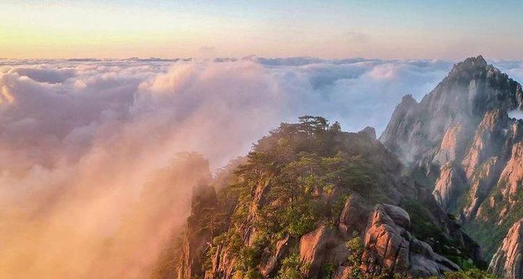 Mountain peaks emerging from clouds at sunrise.