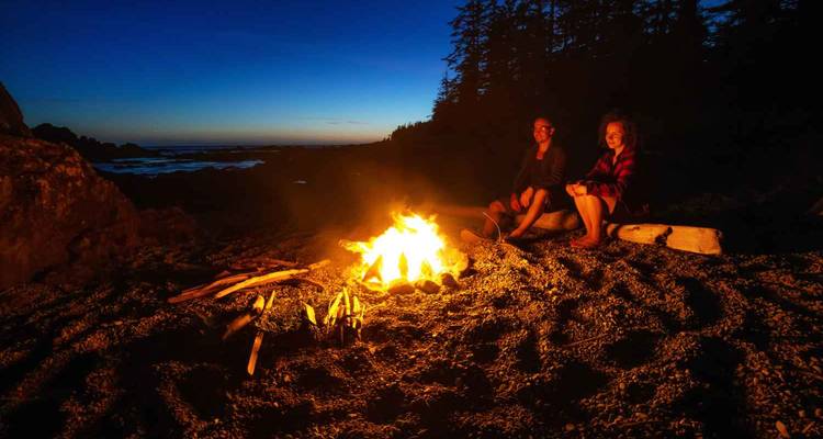 Deux personnes assises près d'un feu de camp sur une plage au crépuscule.