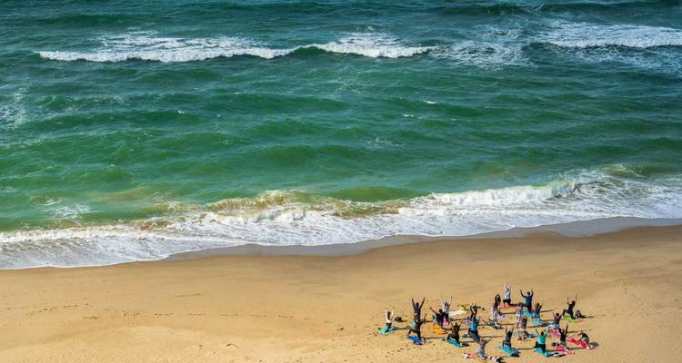 Groupe pratiquant le yoga sur une large plage de sable à côté de vagues vertes ondulantes.