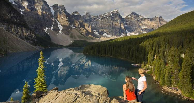Zwei Menschen mit Blick auf eine atemberaubende See- und Berglandschaft.
