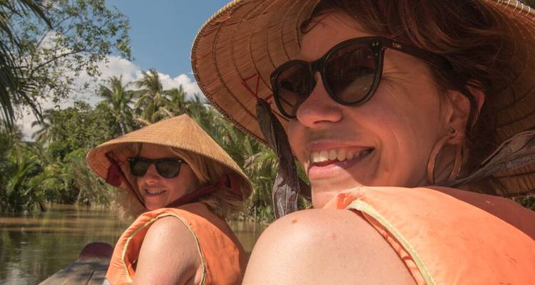 Des gens vêtus de chapeaux traditionnels souriant lors d'une excursion en rivière.