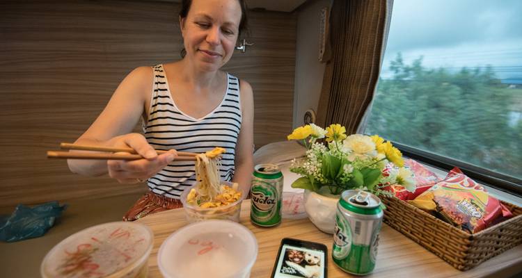 Femme savourant un repas dans un train avec des canettes de boisson.