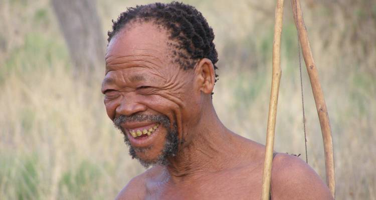 Elderly man smiling, holding a stick, outdoors.