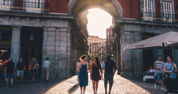 Three people walking through a sunlit archway in a pedestrian street.